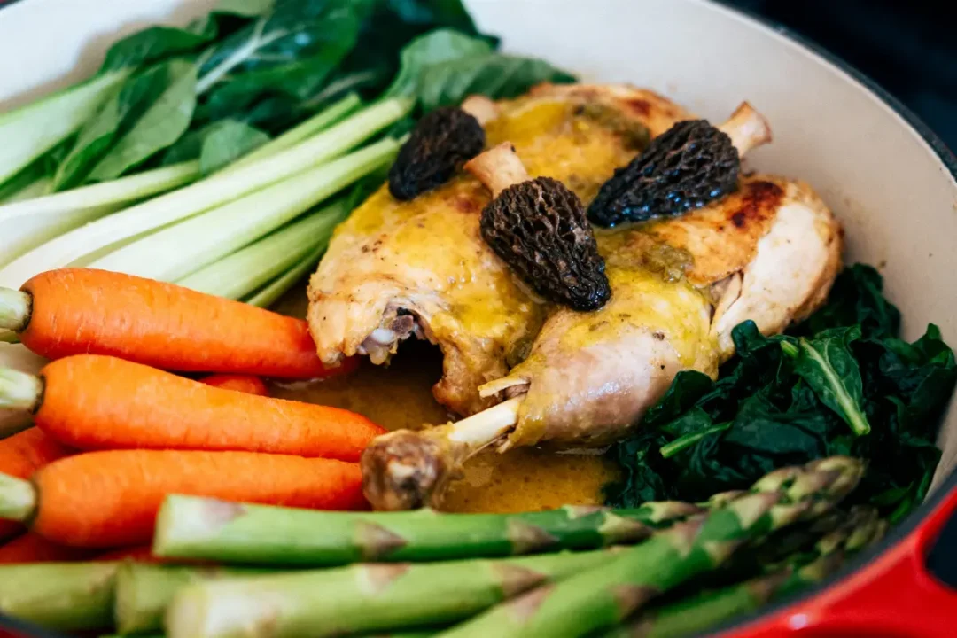 Plat de poulet cuit avec morilles, carottes, asperges et légumes verts dans une cocotte.