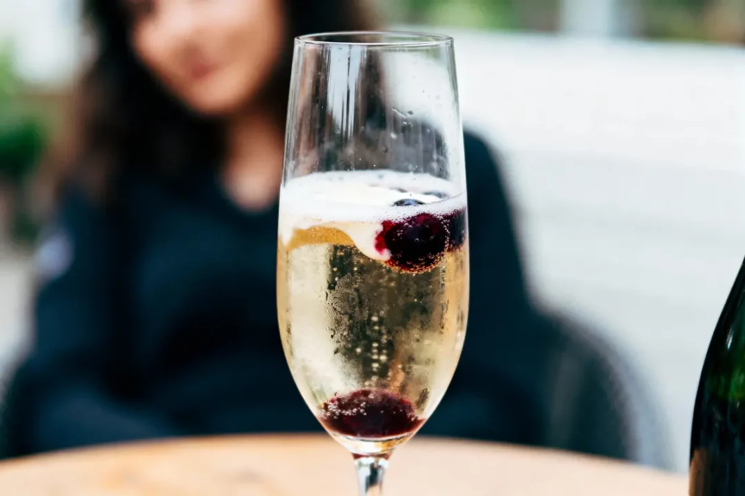 Verre de champagne avec fruits rouges, femme floue en arrière-plan, ambiance élégante.