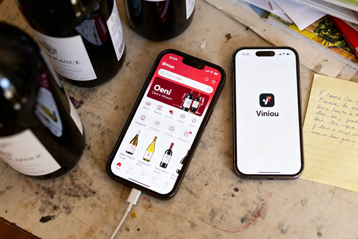 Deux smartphones sur table affichent applications Oeni et Viniou, avec bouteilles de vin et notes manuscrites.