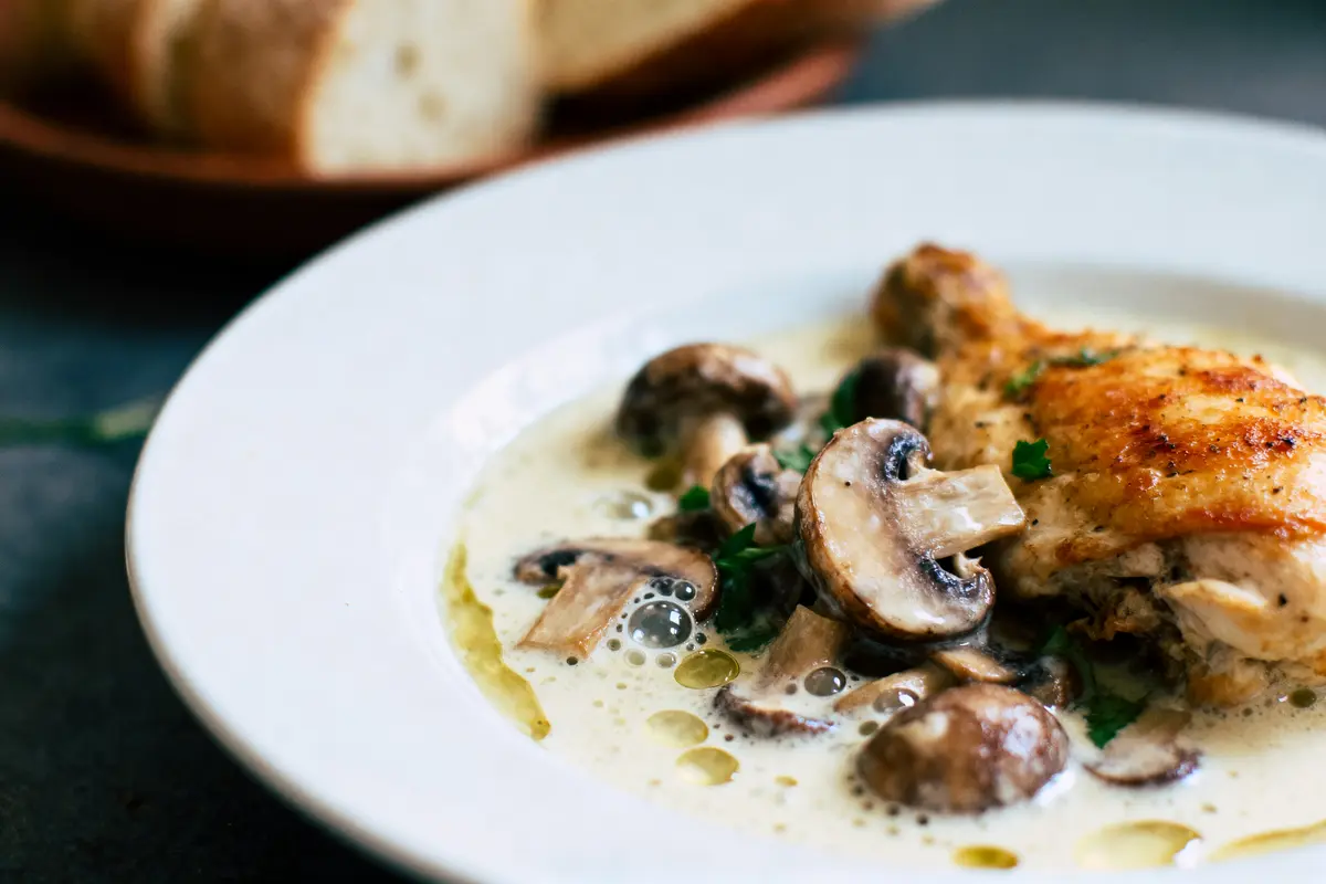 Poulet rôti avec champignons et sauce crémeuse dans une assiette blanche, pain en arrière-plan.