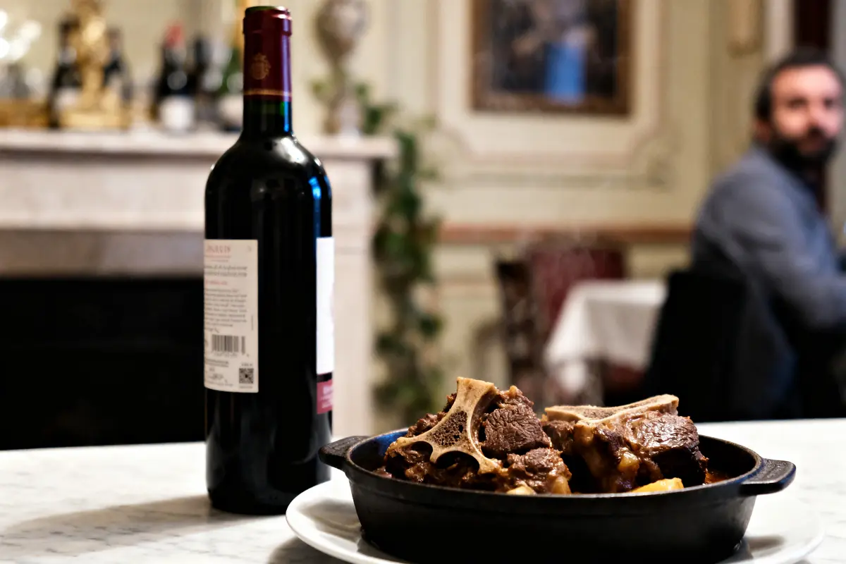 Bouteille de vin rouge et plat de viande braisée sur une table en marbre, homme assis en arrière-plan.