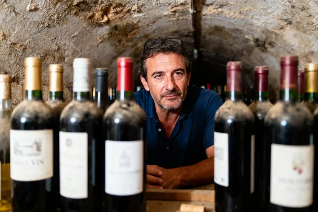 Homme dans une cave à vin entouré de bouteilles de vin poussiéreuses.