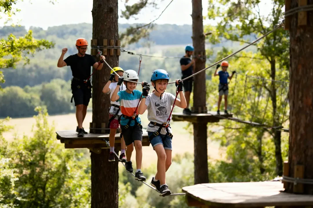 Enfants avec casques et harnais traversant parcours d'accrobranche en forêt, encadrés par un adulte.
