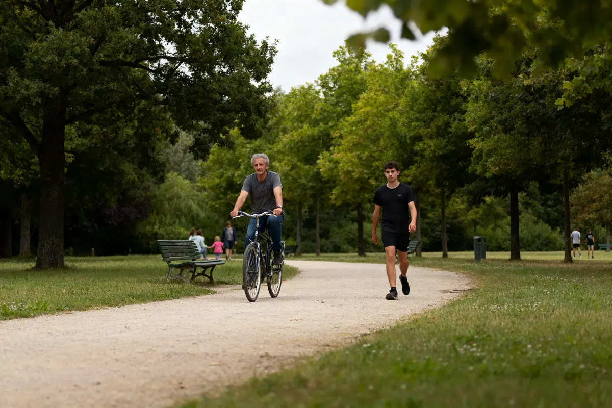 Un homme à vélo et un homme marchant sur un sentier dans un parc verdoyant.