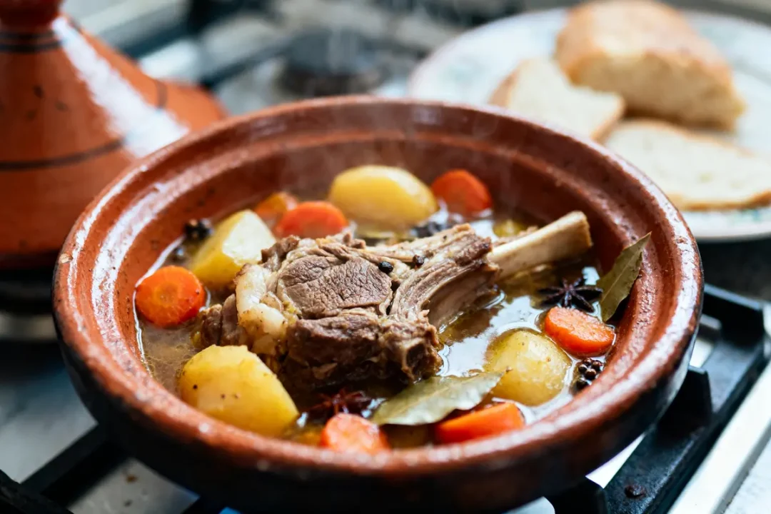 Plat de tajine marocain avec agneau, carottes, pommes de terre, épices, dans un plat en terre cuite.