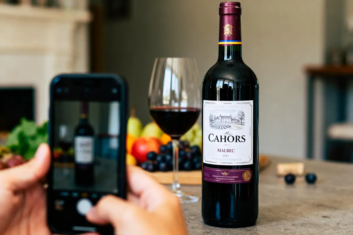 Bouteille de vin rouge Cahors Malbec 2011, verre plein, smartphone photographie, fruits en arrière-plan.