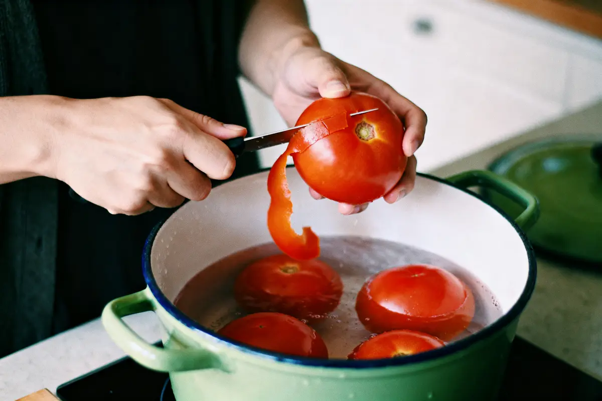 Personne pelant tomate avec couteau au-dessus d'une casserole d'eau pour apprendre comment peler des tomates