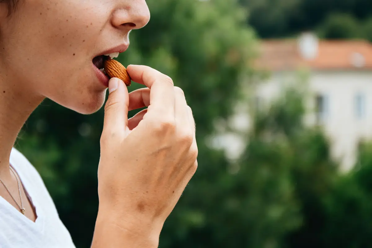 Personne mangeant une amande, attention à manger trop d’amandes pour la santé