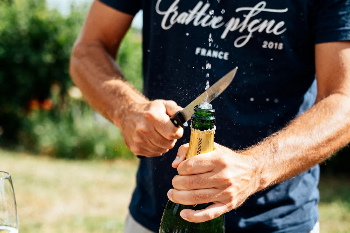 Homme sabrant le champagne avec un couteau, plein air ensoleillé, geste festif.