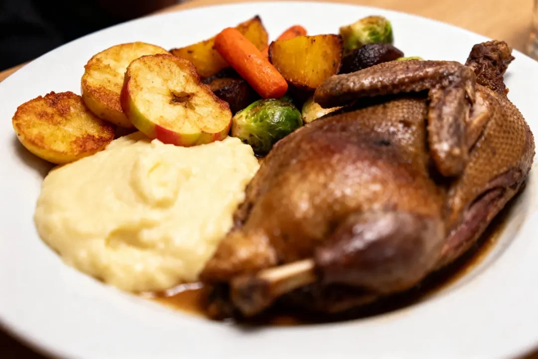 Assiette avec canard rôti, purée, pommes de terre, pommes, choux de Bruxelles, carottes rôties. Repas appétissant.