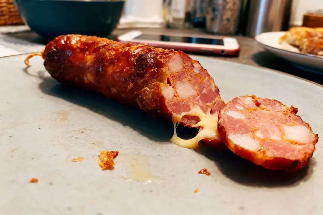 Saucisson avec fromage fondu sur assiette, accompagné d'objets en arrière-plan flou.